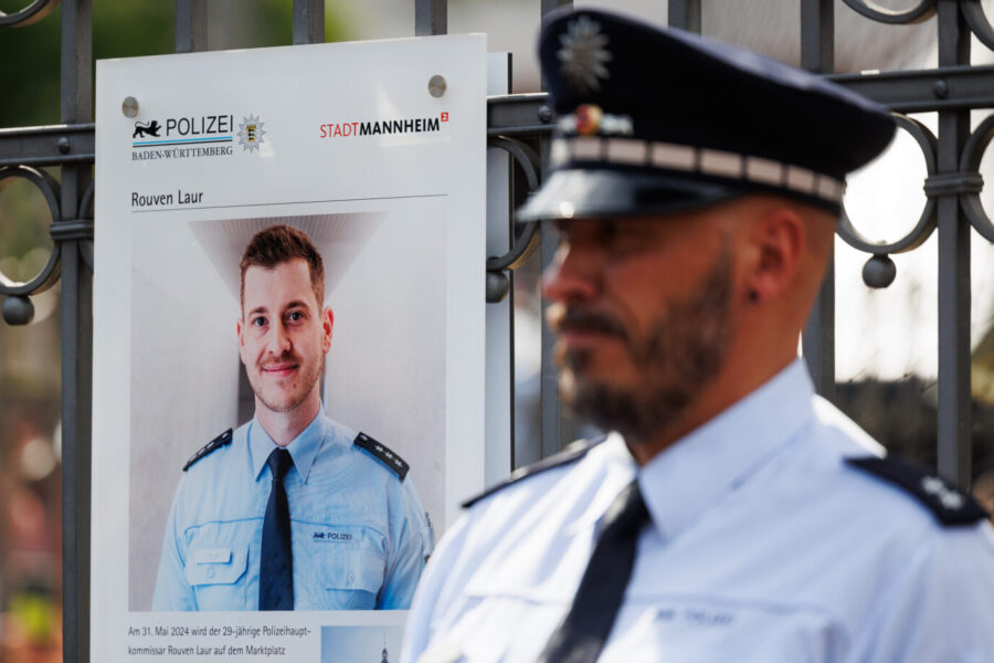 Ein Polizist steht neben einer Gedenktafel mit dem Porträt des getöteten Beamten Rouven Laur.Die Aufnahme entstand bei einer öffentlichen Gedenkveranstaltung der Stadt Mannheim am ersten Jahrestag des tödlichen Messerangriffs auf den Polizeihauptkommissar. Ein Polizist steht neben einer Gedenktafel für Rouven Laur: Die Stadt Mannheim erinnerte am ersten Jahrestag des tödlichen Angriffs an den ermordeten Polizeihauptkommissar. Foto: picture alliance/dpa | Lando Hass