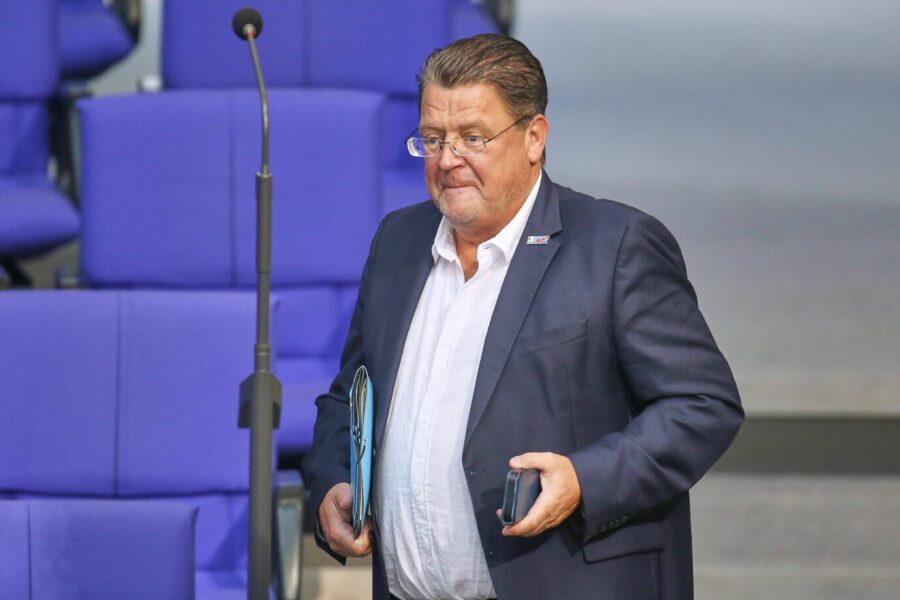 Ein Mann im blauen Sakko mit weißem Hemd steht im Plenarsaal des Bundestages und hält Unterlagen sowie ein Mobiltelefon in der Hand. Fordert die Ausreise der Syrer nach Entfall des Asylgrundes: Stephan Brandner im Bundestag. Foto: IMAGO / dts Nachrichtenagentur