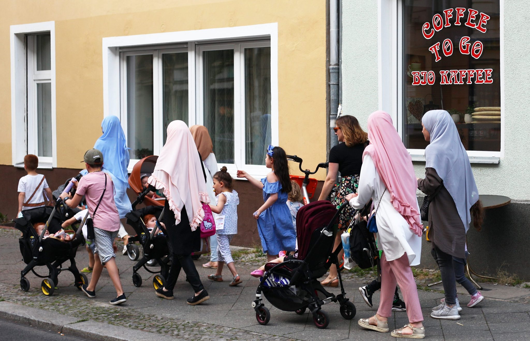 Moslemische Frauen gehen zusammen mit Kindern neben einer deutschen Frau über einen Fußweg in Schöneberg.