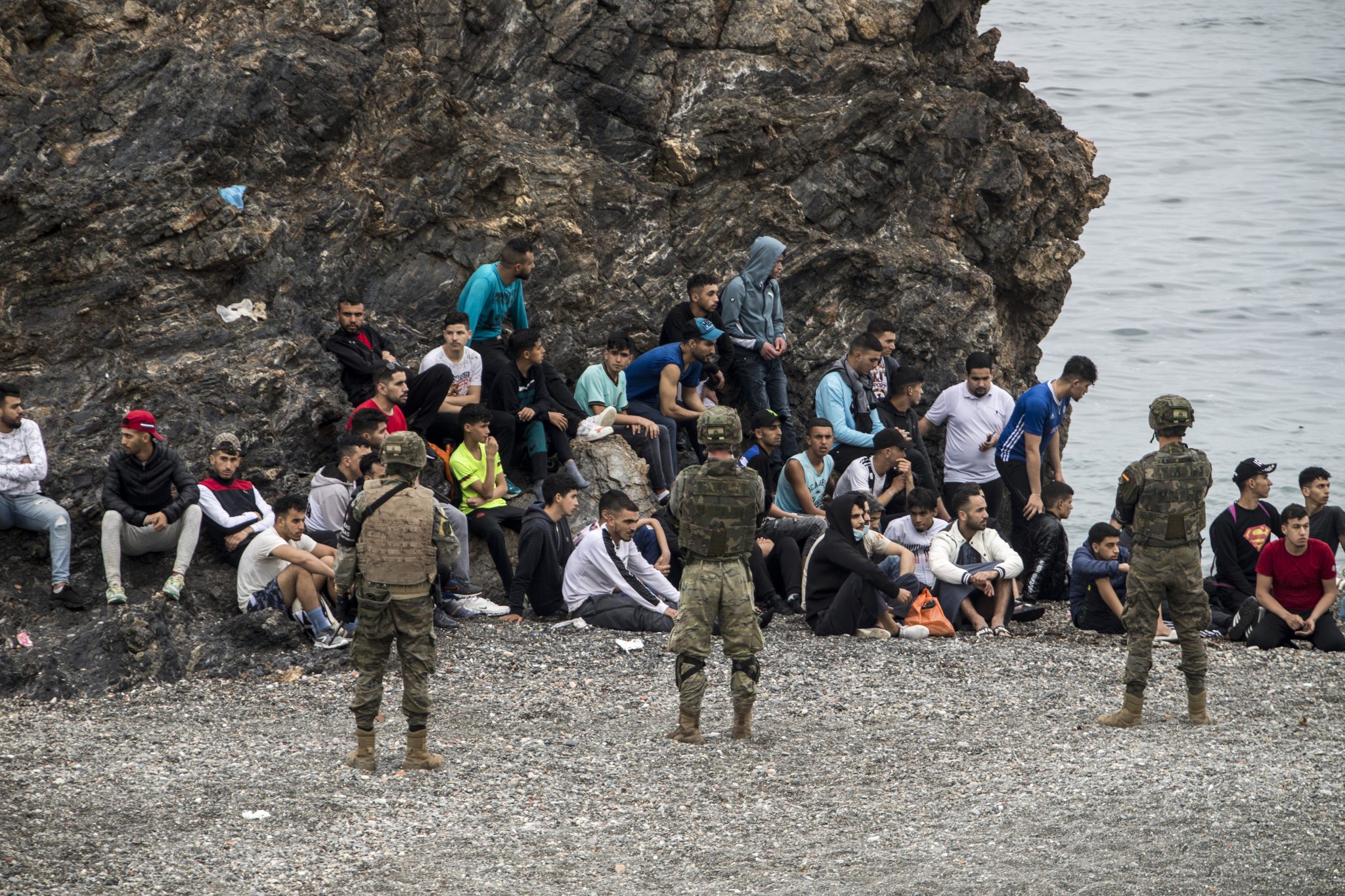 Migranten sitzen vor spanischen Soldaten an der Grenze zwischen Spanien und Marokko