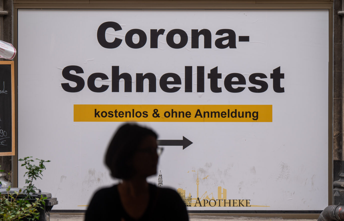 Passantin vor Schild mit Corona-Test-Hinweis in München