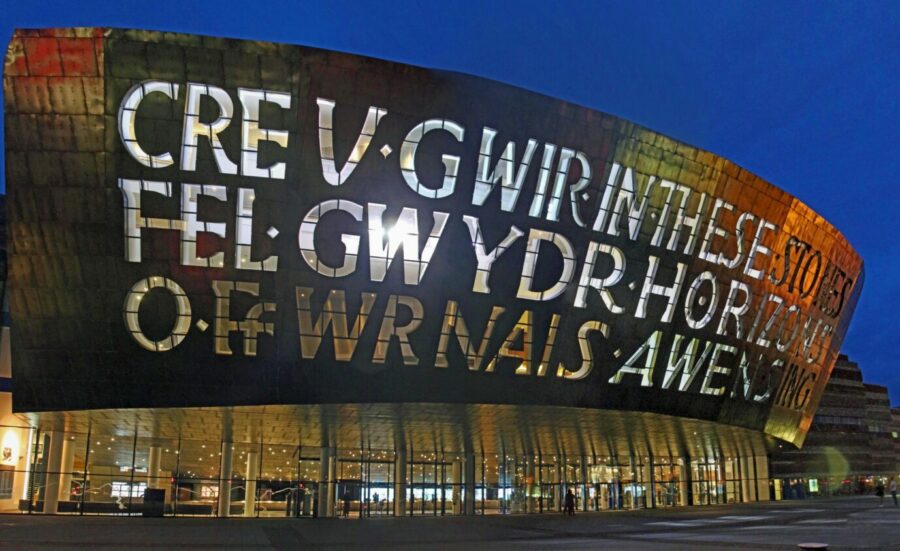 Fassade des Wales Millenium Centre bei Nacht mit der walisischen Inschrift CREU GWIR GWYDR O FFWRNAIS AWEN ("Glas ist so klar wie Glas, geläutert in den Flammen der Inspiration") und der englischen Inschrift “IN THESE STONES HORIZONS SING” Foto: Archiv des Verfassers