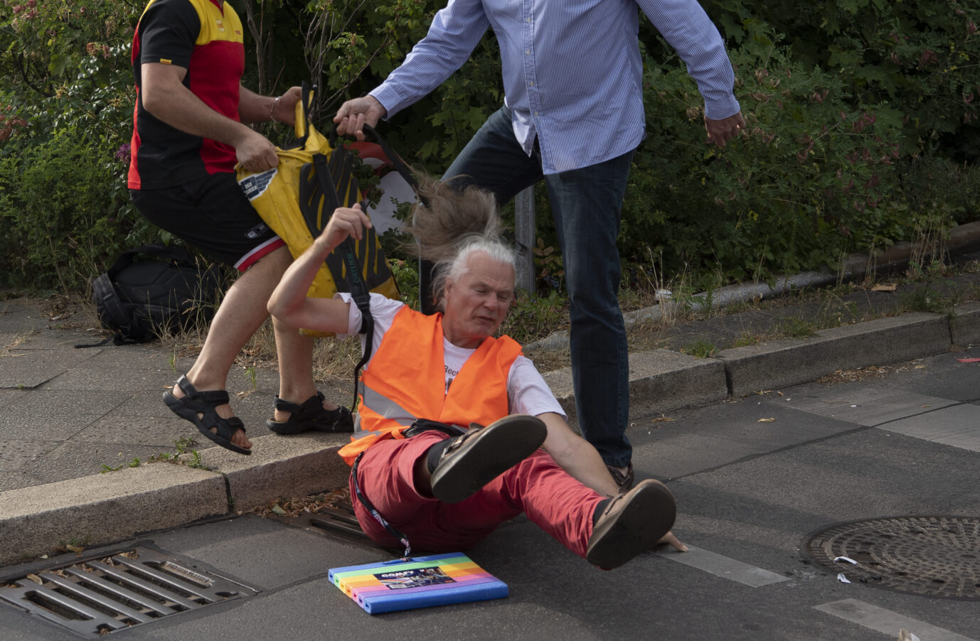 Der erste Verletzte. Ein Mitarbeiter der DHL und ein Autofahrer ziehen einen Demonstranten der Gruppe "Letzte Generation" von der Berliner Autobahn-Ausfahrt.