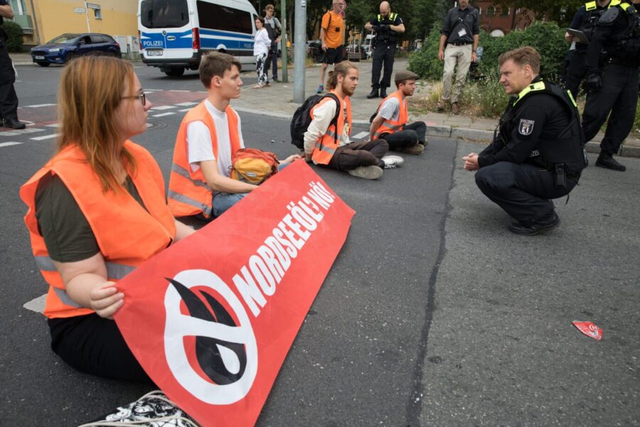 Bevor die Räumung der Straße erfolgt führen Polizisten zunächst Gespräche mit den festgeklebten Blockierern der "Letzten Generation".