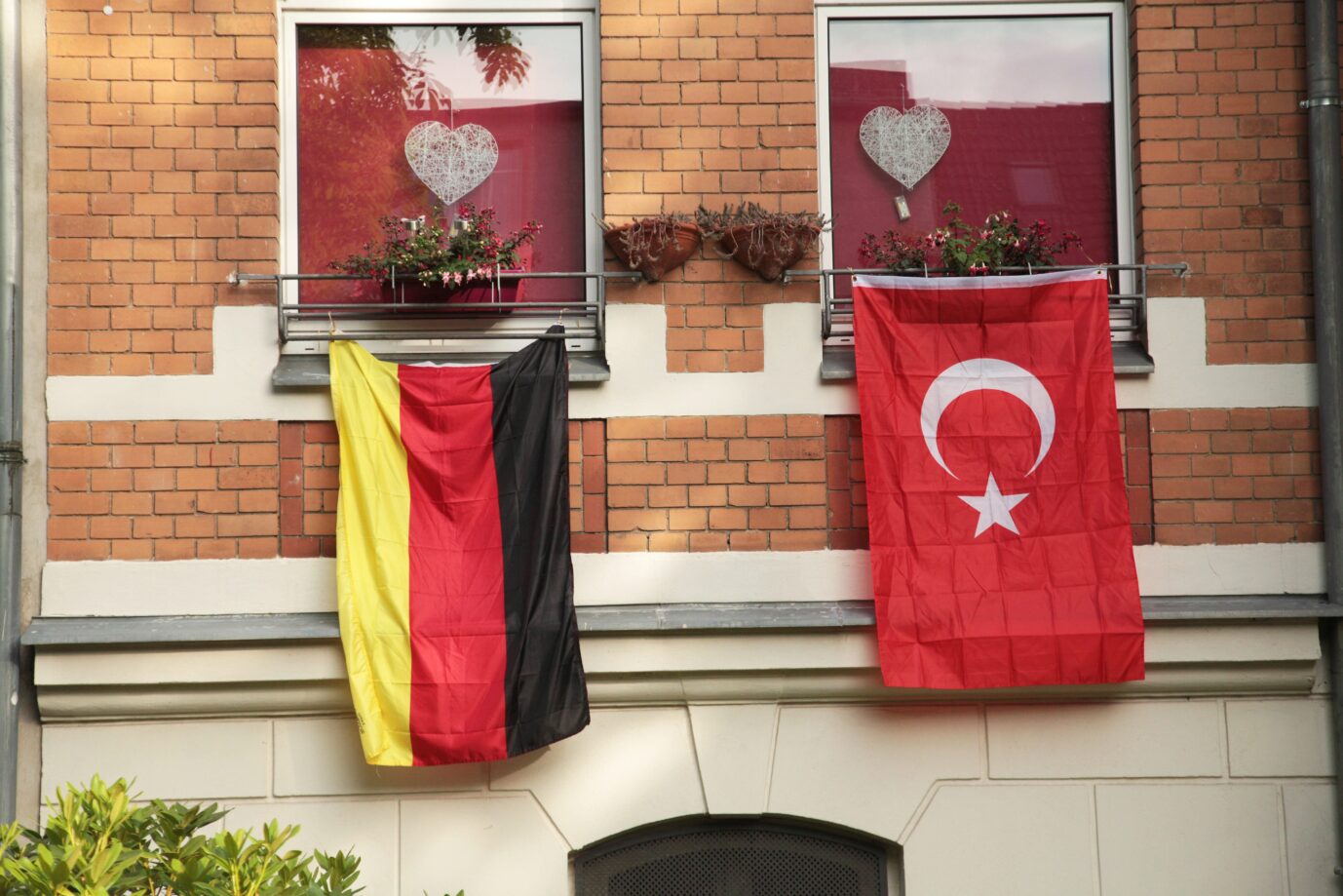 Vor einem Backsteinhaus hängt links eine Deutschlandflagge, rechts daneben hängt eine türkische Flagge. Deutschrap und türkische Begriffe prägen die Sprache der Jugend enorm