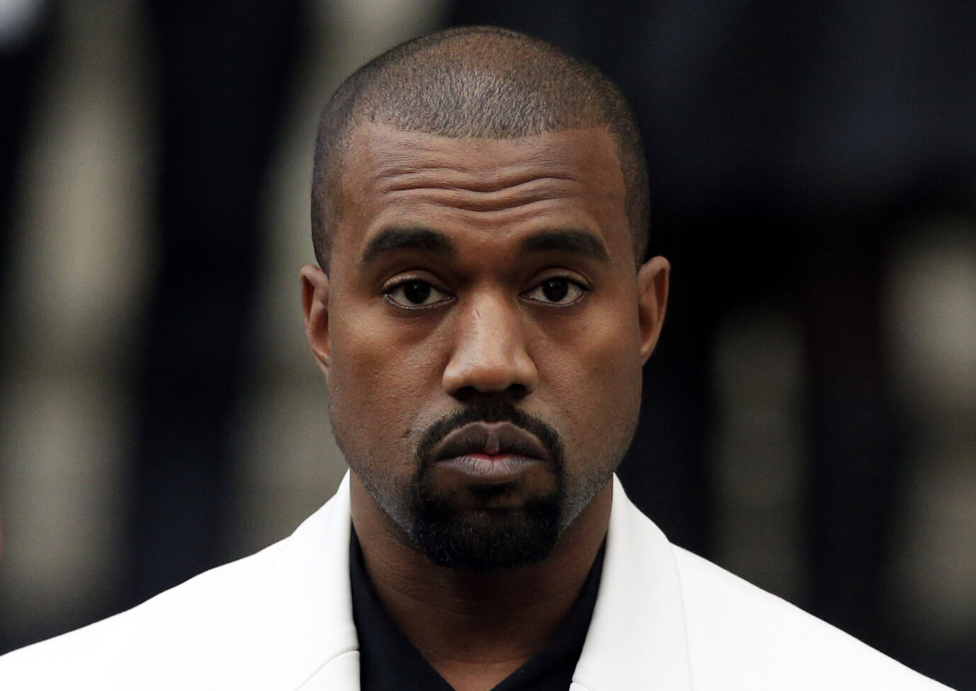 Der US-Rapper Kanye West trägt ein weißes Jackett und schaut frontal in die Kamera.