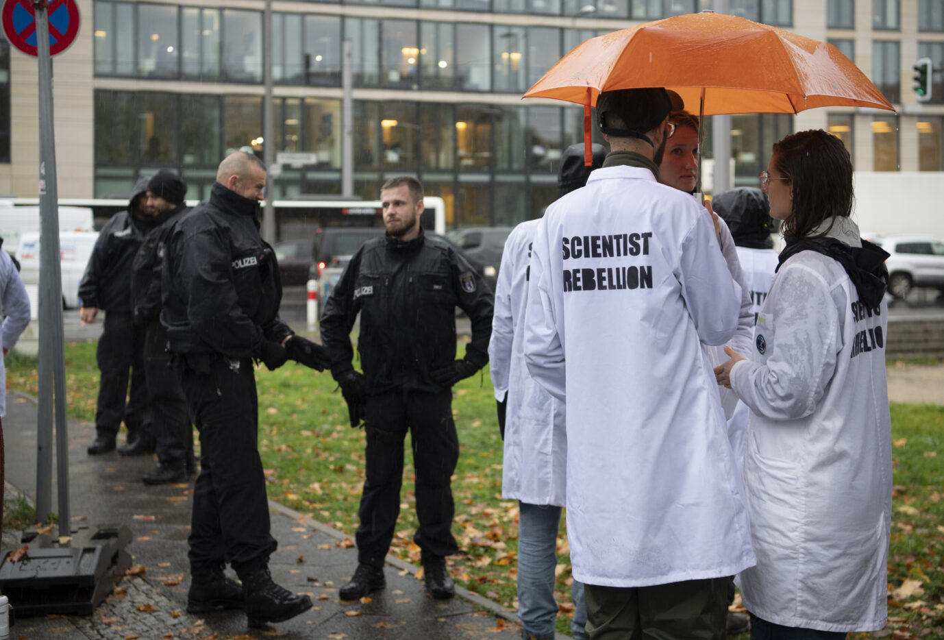 Mitglieder von „Scientist Rebellion“ stehen in weißen Kitteln auf einer grauen Wiese vor dem Bundesverkehrsministerium. Nun demonstrieren die Klima-Kleber in Wolfsburg bei VW.