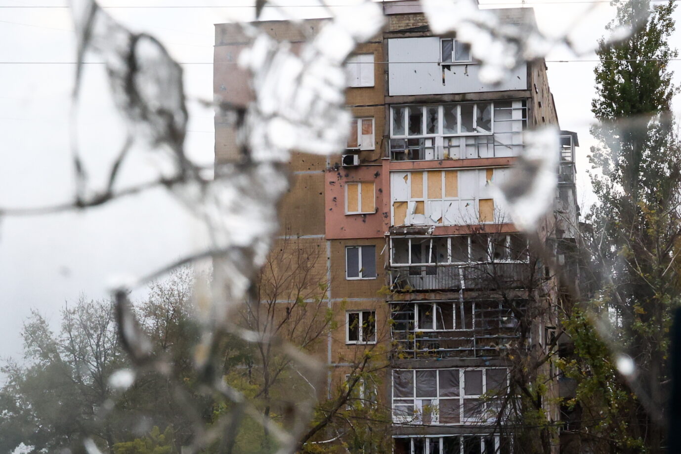 Durch eine zerbrochene Scheibe hindurch ist ein stark beschädigtes Wohnhaus zu sehen. Donezk ist besonders stark vom Krieg zwischen Rußland und der Ukraine betroffen.
