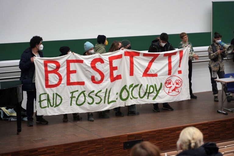 Klimachaoten posieren im Hörsaal der Universität Leipzig mit einem Banner der Gruppe "End Fossil - Occupy".