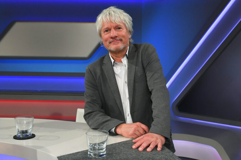 WDR-Kabarettist Jürgen Becker guckt freundlich in die Kamera in einem Fernsehstudio der ARD. Die RAF hält er nicht für so gefährlich wie RWE.