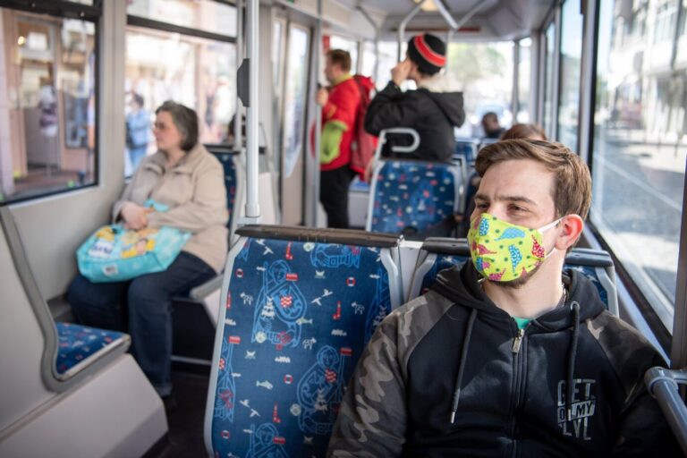 Das Foto zeigt einen Mann mit einer Schutzmaske in einer Straßenbahn. Bremen und Nordrhein-Westfalen beenden fast alle Corona-Maßnahmen ab Februar.
