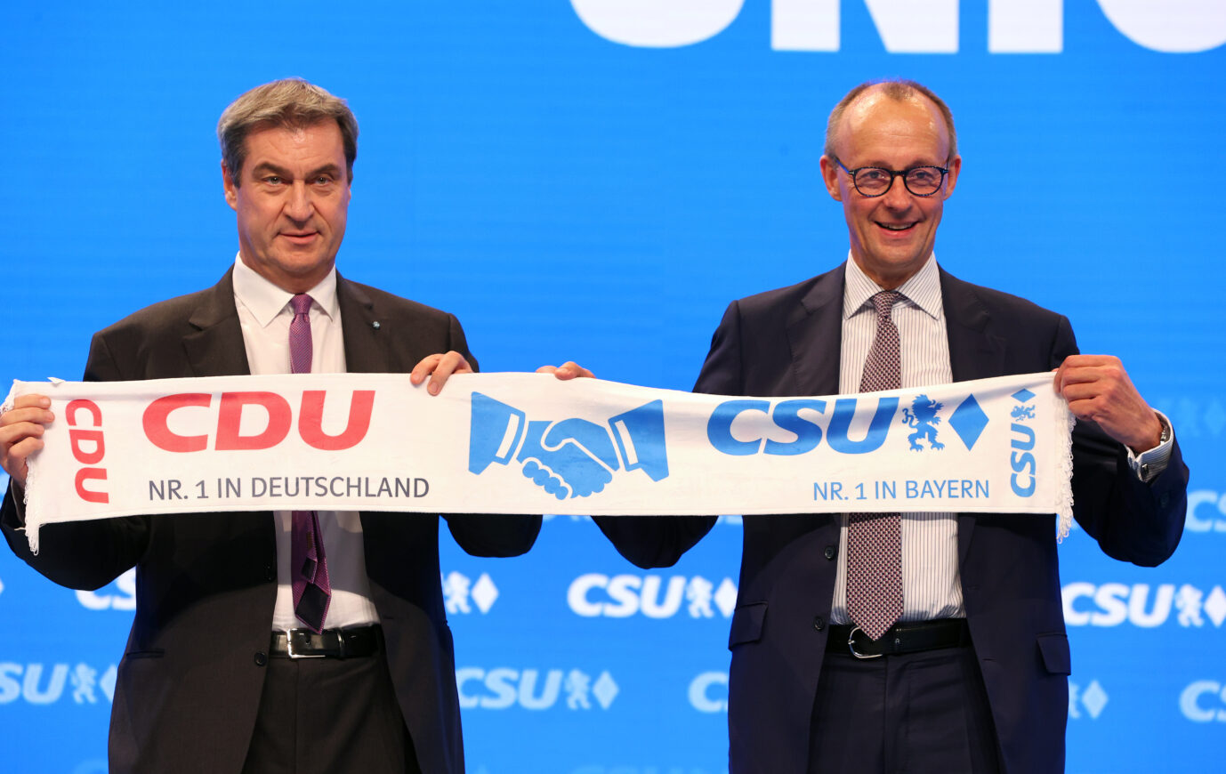 CDU-Parteichef Friedrich Merz (r.) hält zusammen mit Bayerns Ministerpräsident Markus Söder (CSU) gemeinsam einen Parteischal hoch.