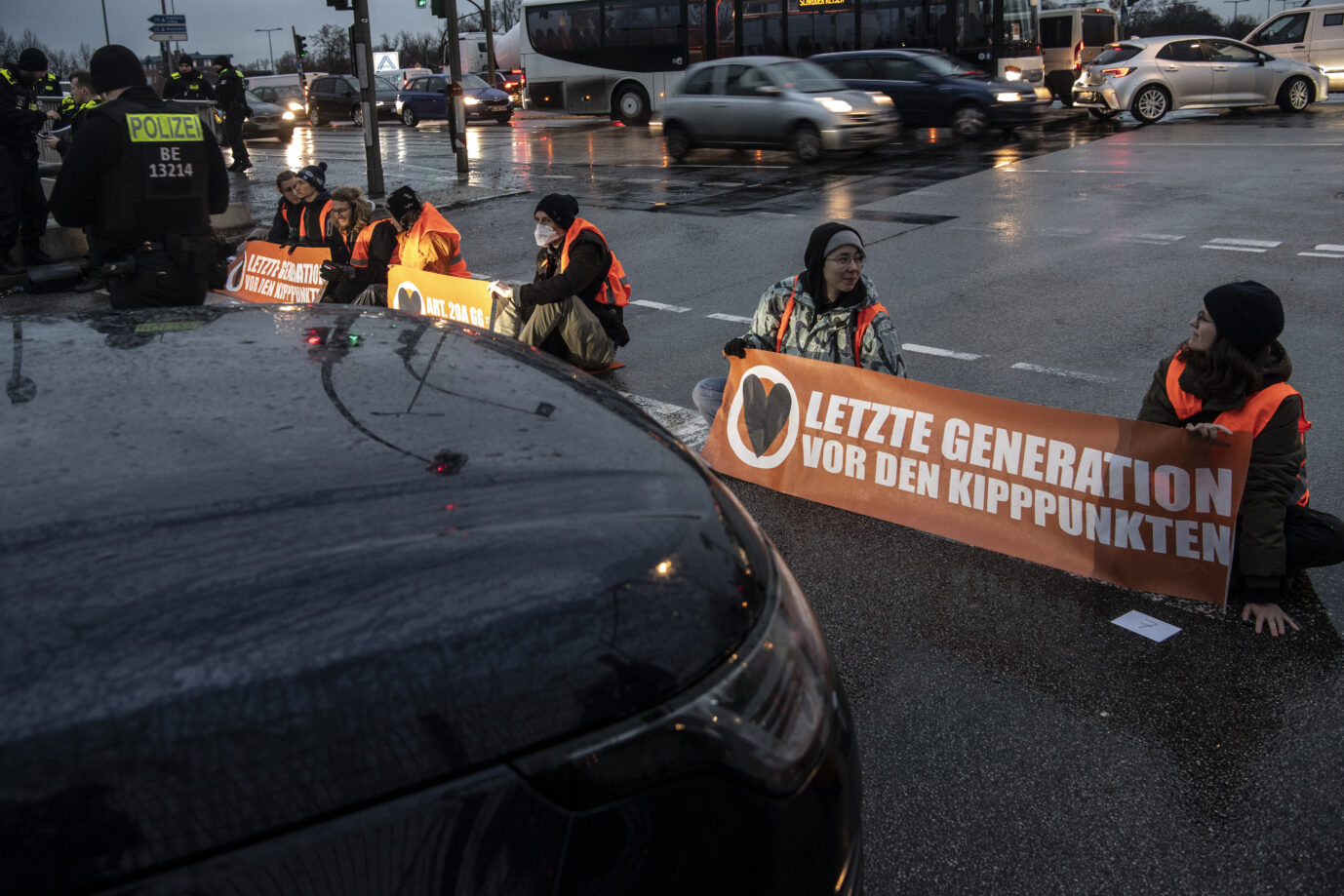 Mitglieder der "Letzten Generation" blockieren immer wieder Straßen in Berlin. Dabei zeigen sie ihre Parolen auf Plakaten. Autofahrer müssen warten.