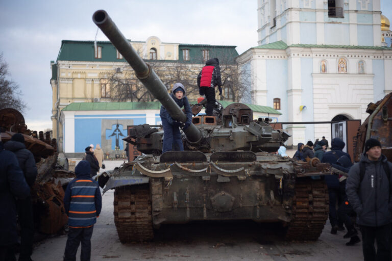 Das Bild zeigt Kinder in der Ukraine, die auf einem in Kiew ausgestellten russischen Panzer spielen.