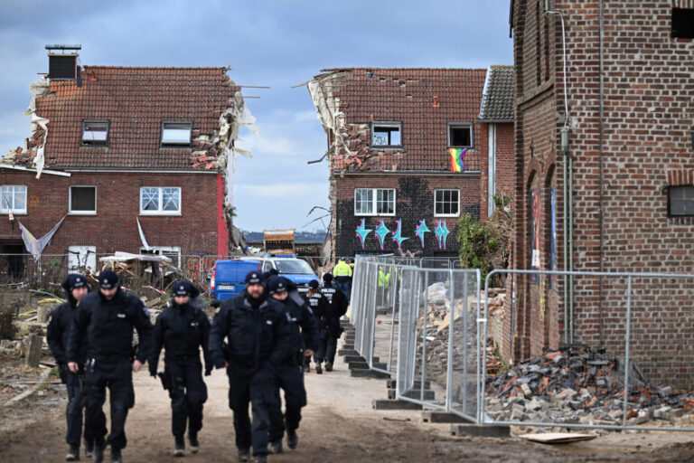 Polizisten gehen durch das geräumte Dorf Lützerath. Hinter ihnen gehen die Abrißarbeiten weiter.