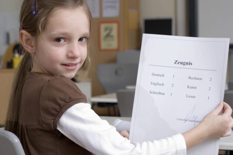 Ein sechsjähriges Mädchen hält ein Schulzeugnis. In Berlin sollen Zeugnisse künftig auf Wunsch ohne „er“ und „sie“ auskommen.