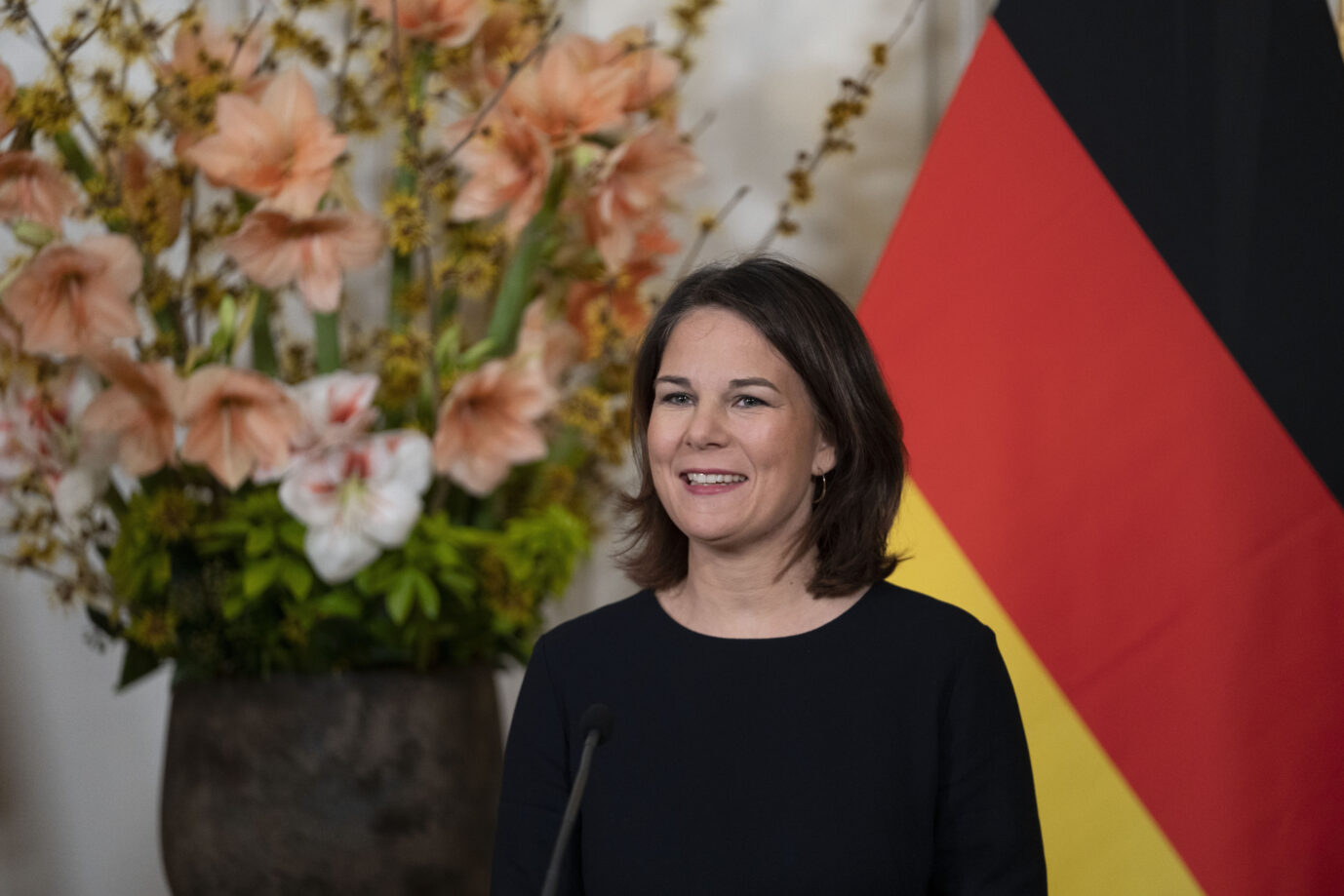 Außenministerin Annalena Baerbock steht vor der Deutschlandfahne und einem Blumenstrauß.