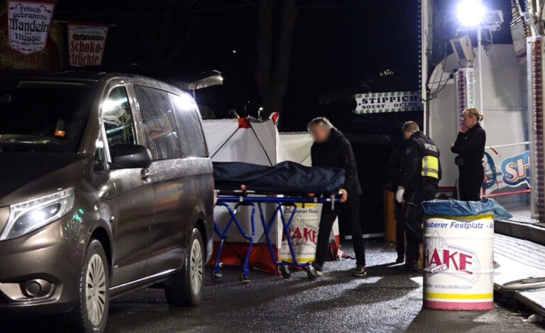 Ein Bestatter bringt den Toten auf der Kirmes in Münster mit einer Bahre in sein Fahrzeug