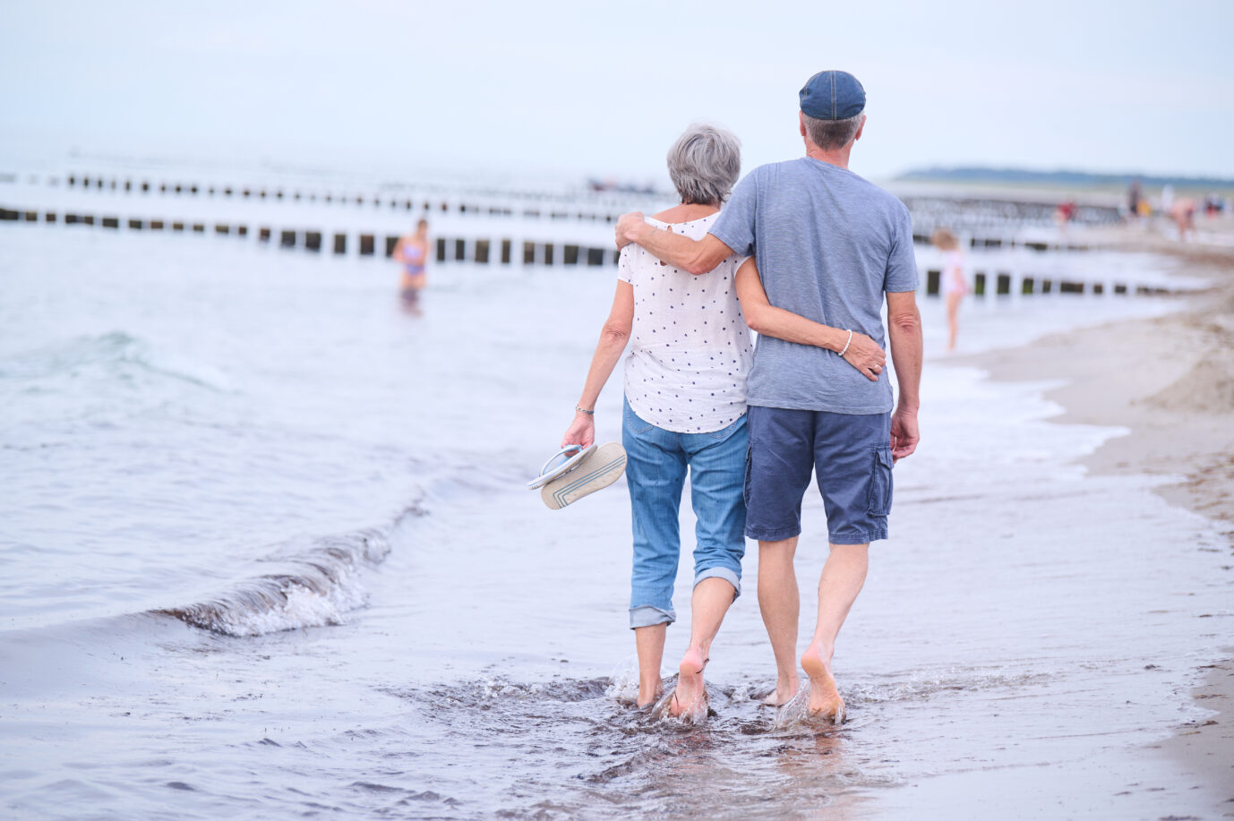 Ein Rentnerehepaar geht barfuß am Strand spazieren. Der Renteneintritt soll sich in Deutschland weiter verspäten.