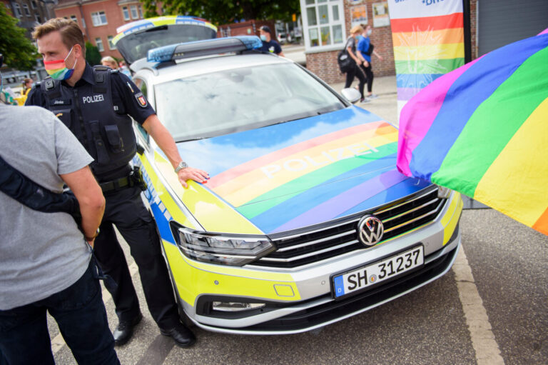 Das Bild zeigt ein deutsches Polizeiauto, das mit Regenbogenfarben dekoriert ist.