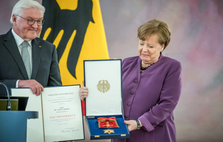 Fremdelt sie schon wieder mit der Farbkombination? Ex-Kanzlerin Angela Merkel schaut skeptisch auf den frisch verliehenen Orden.