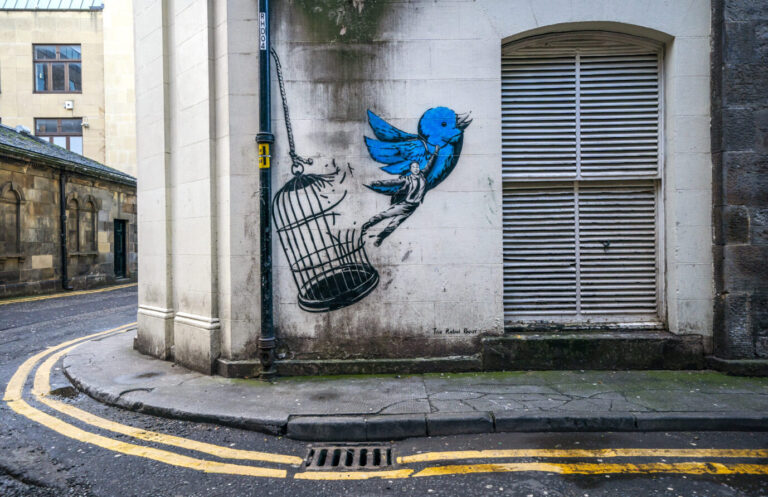Das Bild zeigt ein Streetart-Graffito in Edinburgh. Darauf bricht der Twitter-Vogel aus dem Käfig aus und zieht Elon Musk mit. Die Twitter-Akten haben das Ausmaß der Zensur offengelegt.