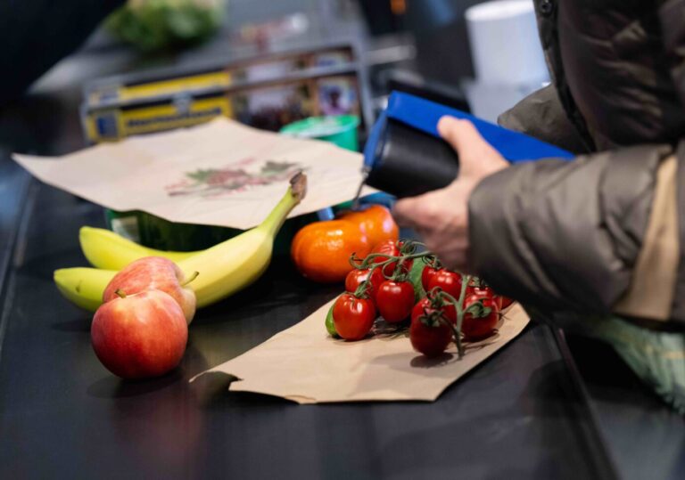 Lebensmittel liegen in einem Supermarkt an der Kasse auf dem Band. Unter dem Eindruck der hohen Inflation rechnen der Einzelhandel mit zurückhaltenden Verbraucherkonsum.