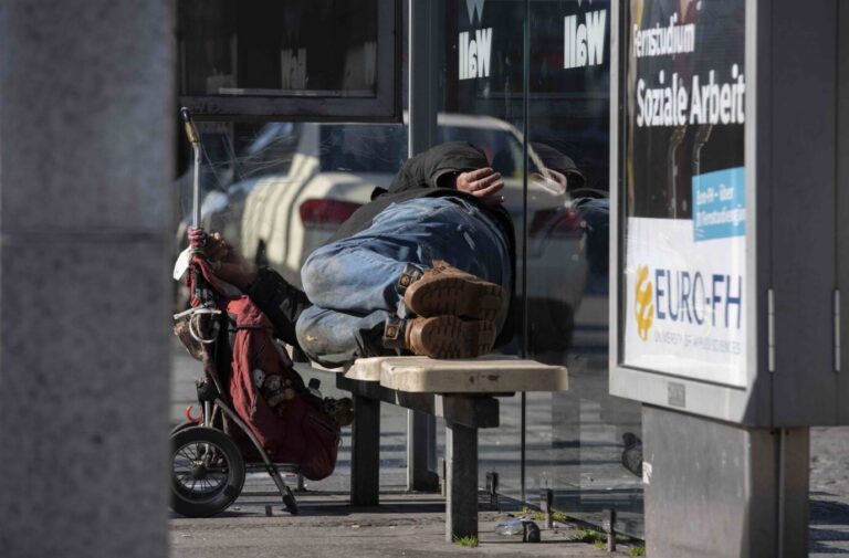 Ein obdachloser Mann liegt in seiner Armut an einer Haltestelle auf einer Bank und schläft.