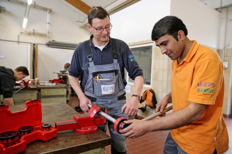 Ein Handwerksmeister leitet seinen Azubi in der Ausbildung beim Schneiden eines Gewindes an.