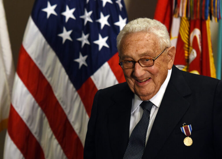 Das Foto zeigt Henry Kissinger vor einer Flagge der USA.