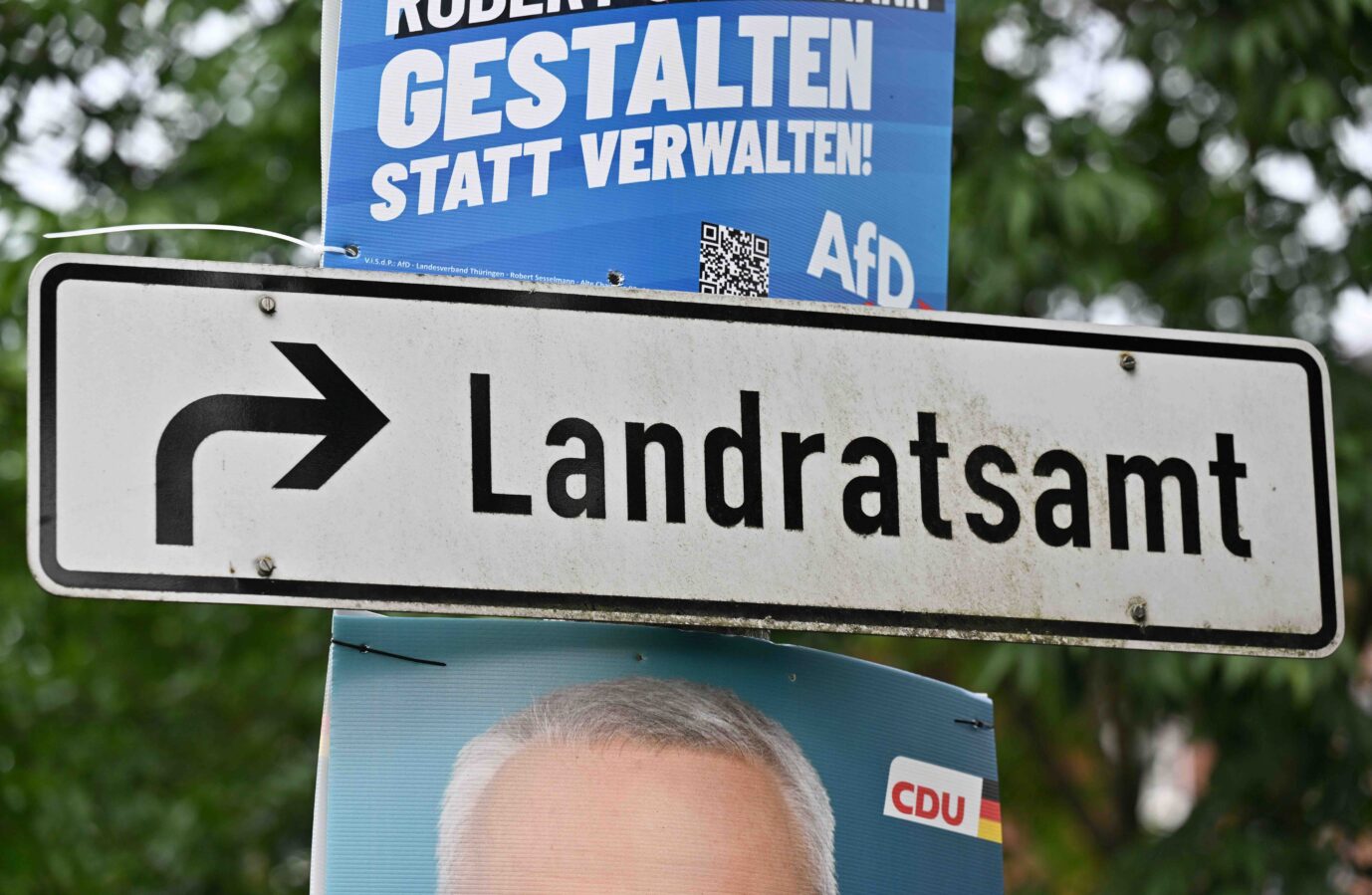 Plakate mit Fotos der Kandidaten hängen neben einem Wegweiser zum Landratsamt. Am 25. Juni findet die Stichwahl für das Amt des Landrats im Landkreis Sonneberg statt. Der amtierende Landrat Jürgen Köpper (CDU) geht in die Stichwahl gegen den AfD-Kandidaten Robert Sesselmann.