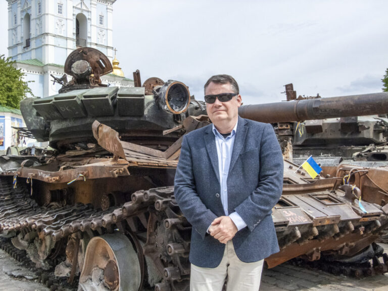 Sven Geschinski steht vor russischem Panzerwrack in Kiew.