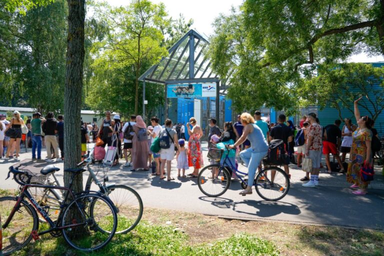 Berlin, das Sommerbad bzw. Columbiabad der Berliner Bäder-Betriebe (BBB) in Neukölln ist derzeit geschlossen. Die offizielle Begründung ist ein hoher Krankenstand bei den Mitarbeitern. Zuletzt kam es in dem Freibad immer wieder zu Gewalt, verbalen Attacken oder Pöbeleien von Besuchern. Die Mitarbeiter beklagen katastrophale Zustände. Im Bild: Der Eingangsbereich des Bades mit Schild und einigen Besuchern die in einer Schlange anstehen. Badehose? Besser nicht einpacken