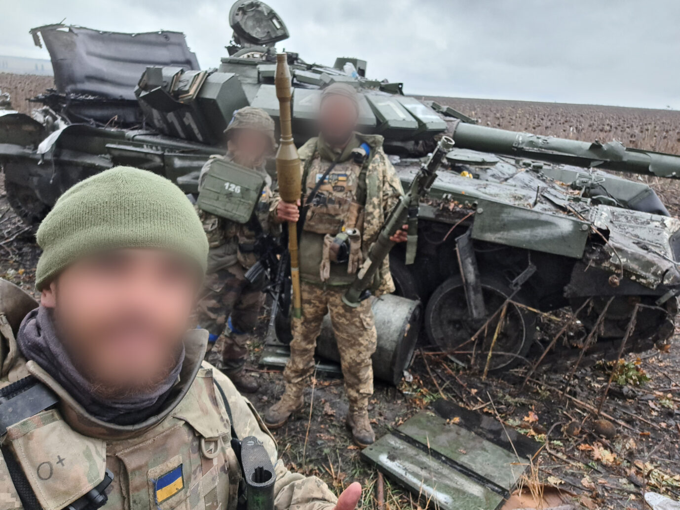 Kolumbianer der Internationalen Legion der Ukraine stehen vor einem abgeschossenen Panzer der Russen.