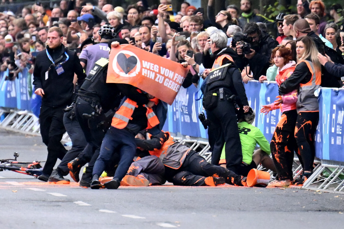 Dieses Bild zeigt eine Szene beim Berliner Marathon. Mitglieder der "Letzten Generation" werden bei einem Störungsversuch, bei dem sie orangefarbene Farbe verschütten, von Polizisten gestoppt.