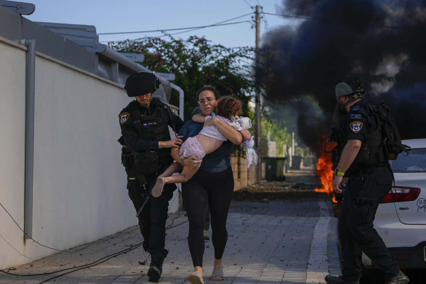 Israeli police officers evacuate a woman and a child from a site hit by a rocket fired from the Gaza Strip, in Ashkelon, southern Israel, Saturday, Oct. 7, 2023. The rockets were fired as Hamas announced a new operation against Israel. (AP Photo/Tsafrir Abayov)