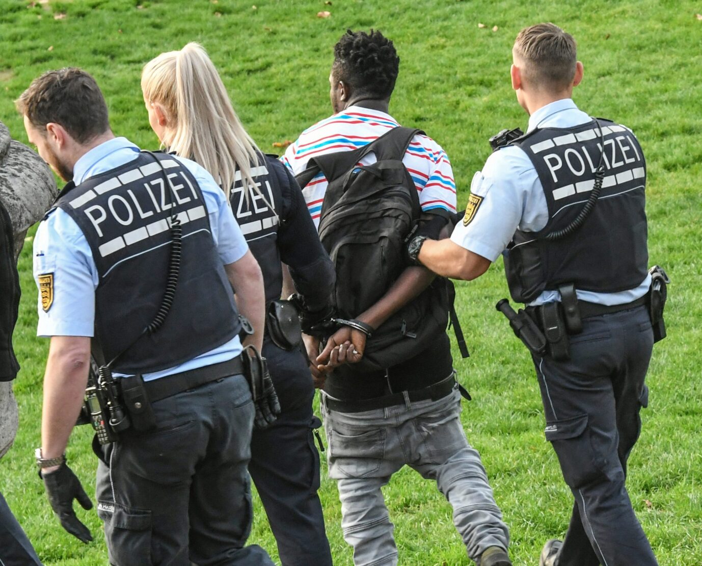 Auf dem Foto befindet sich ein von drei Polizisten festgenommener Schwarzer auf der Wiese. Dieses Bild soll den Aufwand der Polizei im Kampf gegen kriminelle Asylbewerber, Illegale und anerkannte Schutzsuchende verdeutlichen. (Symbolbild)