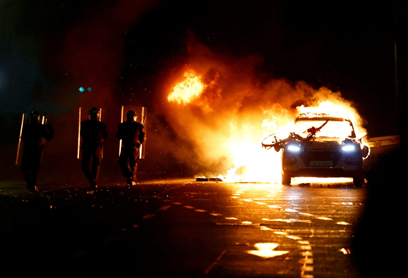 Iren in Irland: Irische Polizisten gehen an einem brennenden Fahrzeug vorbei, Dublin 23. November 2023