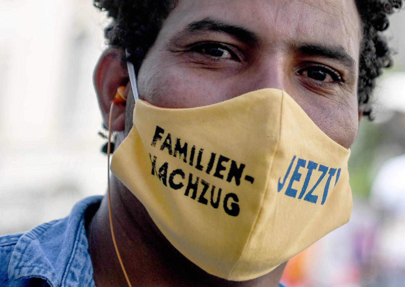 Ein junger Mann trägt einen Mundschutz mit der Aufschrift "Familiennachzug Jetzt". Bei einer Demonstration wird der Familiennachzug gefordert.
