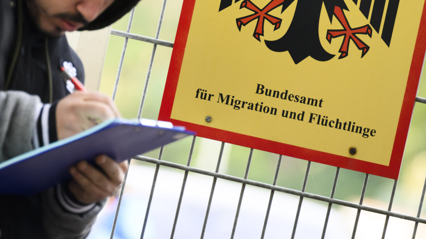 Ein Mann steht vor dem Bundesamt für Migration und Flüchtlinge und füllt ein Dokument aus: Der Zuzug nach Deutschland hält weiter an.