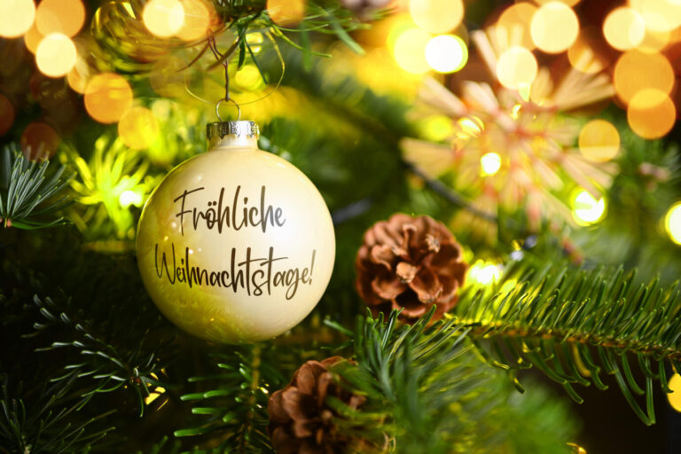 Weihnachtskugel mit Aufschrift Fröhliche Weihnachtstage hängt an einem Weihnachtsbaum, Fotomontage