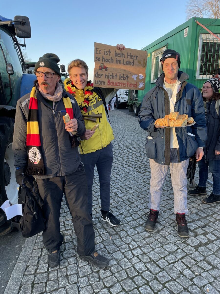 Landwirte verteilen bei der Bauerndemo in Berlin Brötchen um bei Kräften zu bleiben. Einer hält ein Schild hoch auf dem steht „Es ist kein Herr so hoch im Land, der nicht lebt vom Bauernstand“ Foto: Martina Meckelein | JF