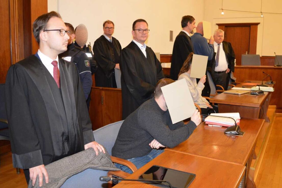 Zwei der angeklagten Polizisten verdecken im Dortmunder Gerichtssaal ihre Gesichter.