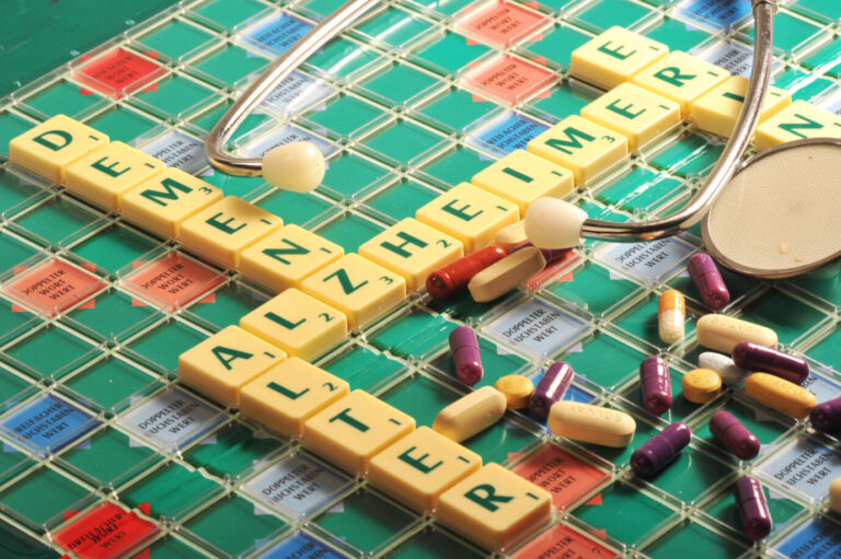 Die Begriffe „Alzheimer“ und „Demenz“ auf einem Scrabble-Brett mit Tabletten: Die Ursachen für Alzheimer werden seit Langem intensiv untersucht.