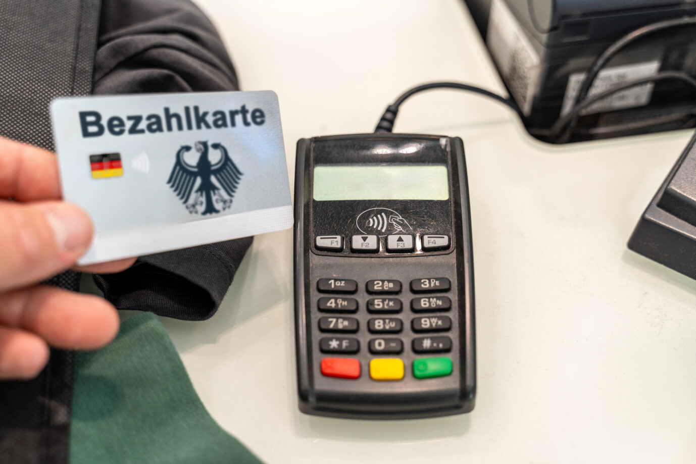 Ein Mann hält eine EC-Karte mit Deutschland Landesfarben, Bundesadler und der Aufschrift: Bezahlkarte vor ein Kartenlesegerät in einem Geschäft. Die Bezahlkarte soll Deutschlandweit an Asylbewerber ausgegeben werden FOTOMONTAGE