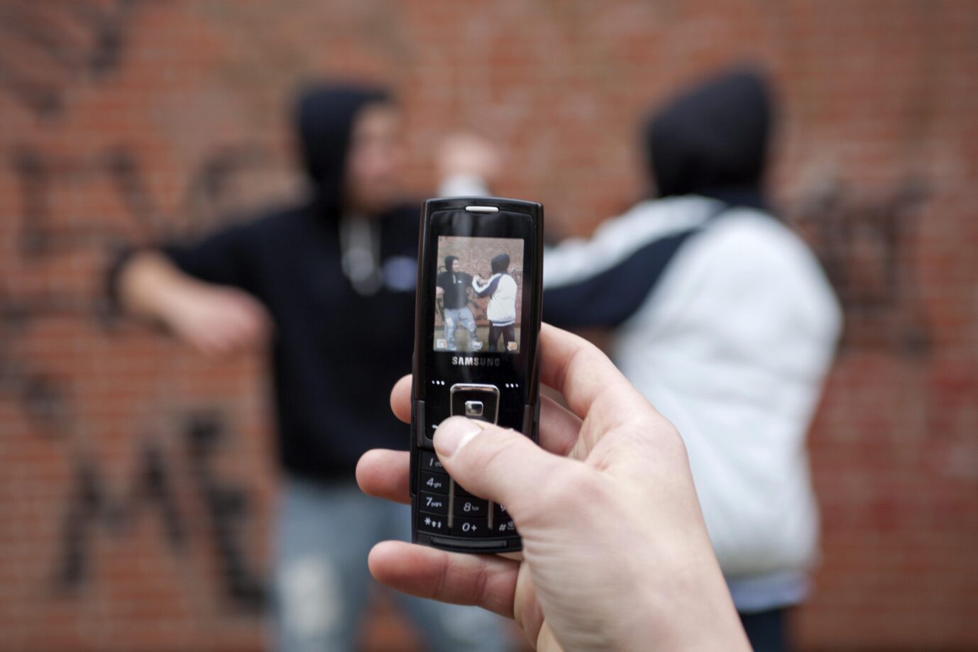 Auf dem Foto befindet sich eine Szene, bei der eine Person mit einem klassischen Mobiltelefon zwei Schüler bei einem Gewaltexzess aufnimmt. (Themenbild/Symbolbild)