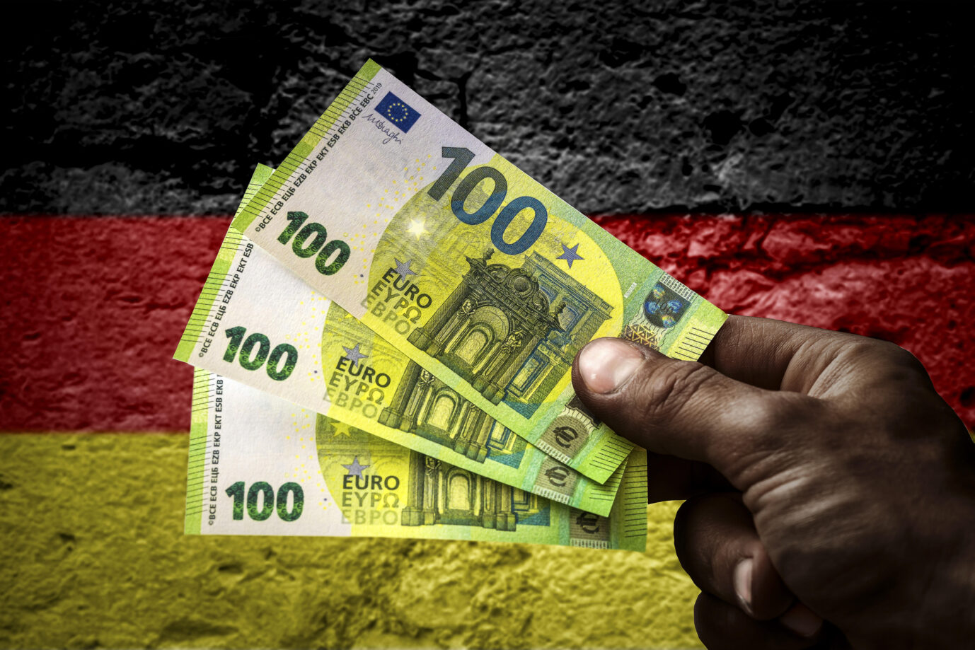 Hand von einem Asylbewerber hält mehrere hundert Euro Geldscheine vor einer Deutschland Flagge. Symbolbild Geld und Sachleistungen für Geflüchtete FOTOMONTAGE Jetzt geht es um Scheinvaterschaften.