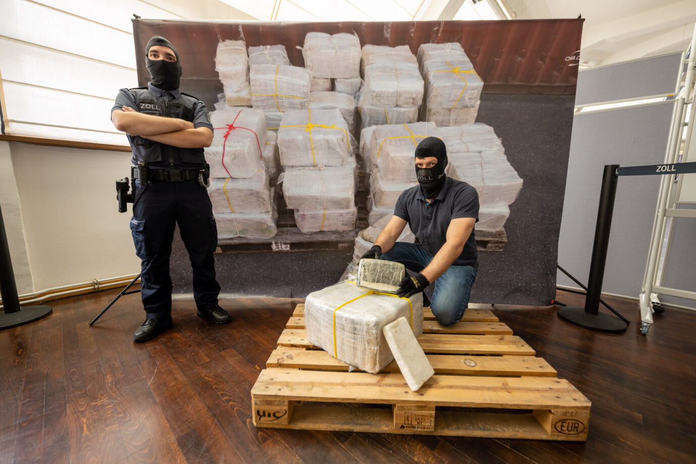 Zwei maskierte Polizeibeamte knien und stehen vor einem sichergestellten Kokainfund