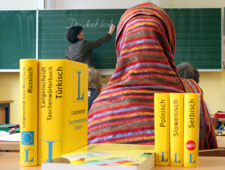 Ein junges Mädchen mit einem roten Kopftuch sitzt in einer Grundschulklasse, daneben stehen mehrere Duden. Eine Lehrerin schreibt "Deutschtest" an die Tafel – es könnte eine typische Szene in der Gräfenauschule sein. Dort bleiben 44 Erstkläßler sitzen.