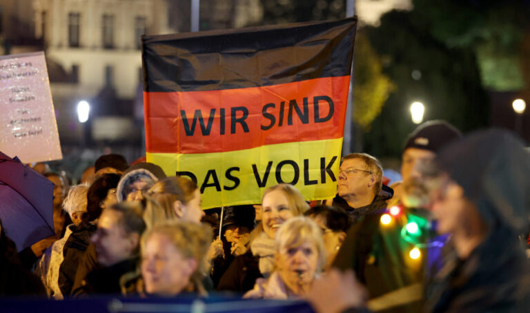 Demonstranten halten eine Deutschlandfahne mit der Aufschrift "Wir sind das Volk" hoch, Grundgesetz